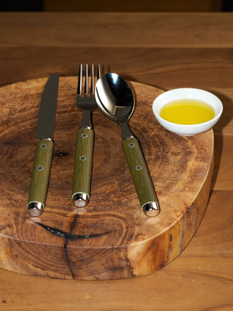 Posate con manico in legno d'ulivo su un tagliere rustico accanto all'olio