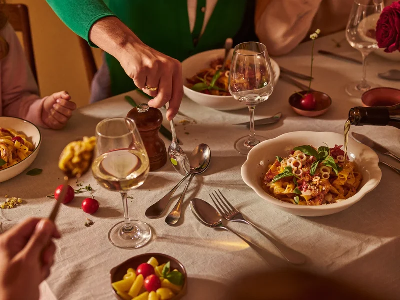 Tavola familiare festiva vista dall'alto con posate, pasta e bicchieri da vino